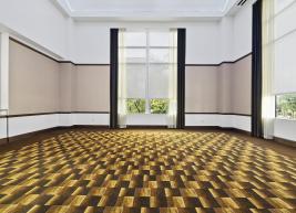 A photo of the lounge before, shown is an empty room with pattern carpet and tan and white walls